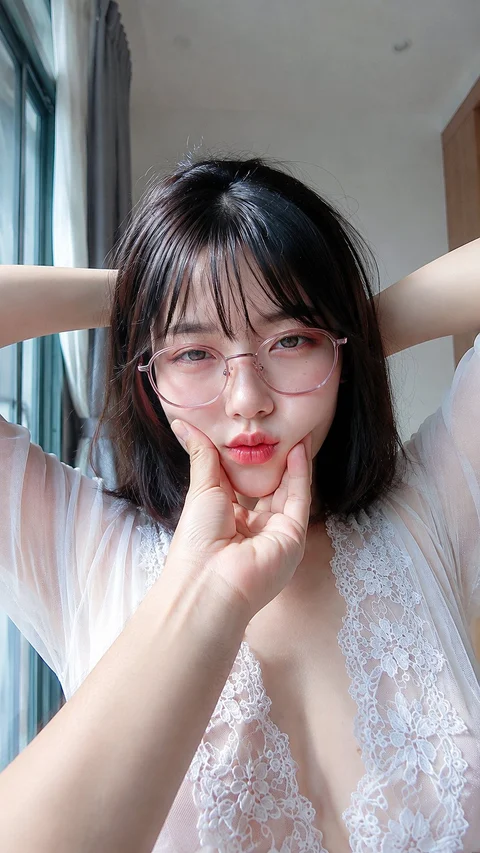 A woman with a short dark bob and glasses poses with a fingertip near her lips.